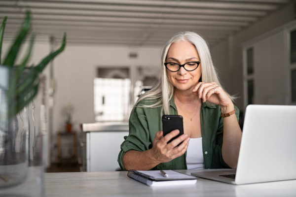 Happy senior woman using mobile phone while working at home with