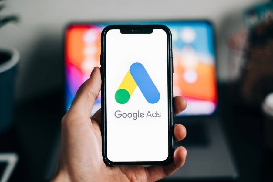 Person holding a smartphone in front of a computer showing google ads logo